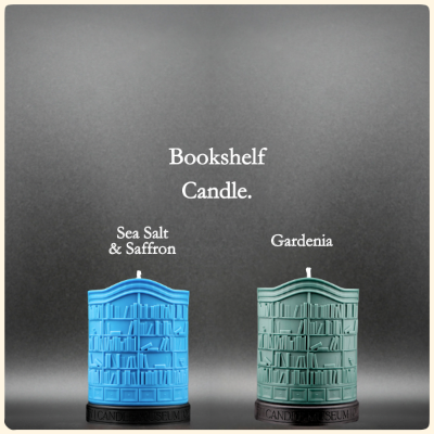 Two bookshelf-shaped candles, one blue and one green, on a gray background with text indicating scents.