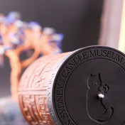 Candle with 'Sydney Candle Museum' branding and a cat silhouette on a blurred background