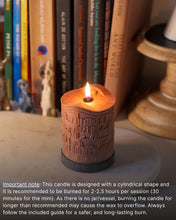 A cylindrical brown candle with a printed book spine design and a visible flame, placed on a tabletop in front of books, with a candle holder partially visible on the right and a text note at the bottom.
